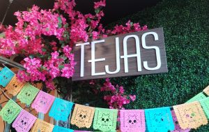 A sign surrounded by papel picado, a special paper used to decorate for celebrations in Mexico such as Día de los Muertos. 